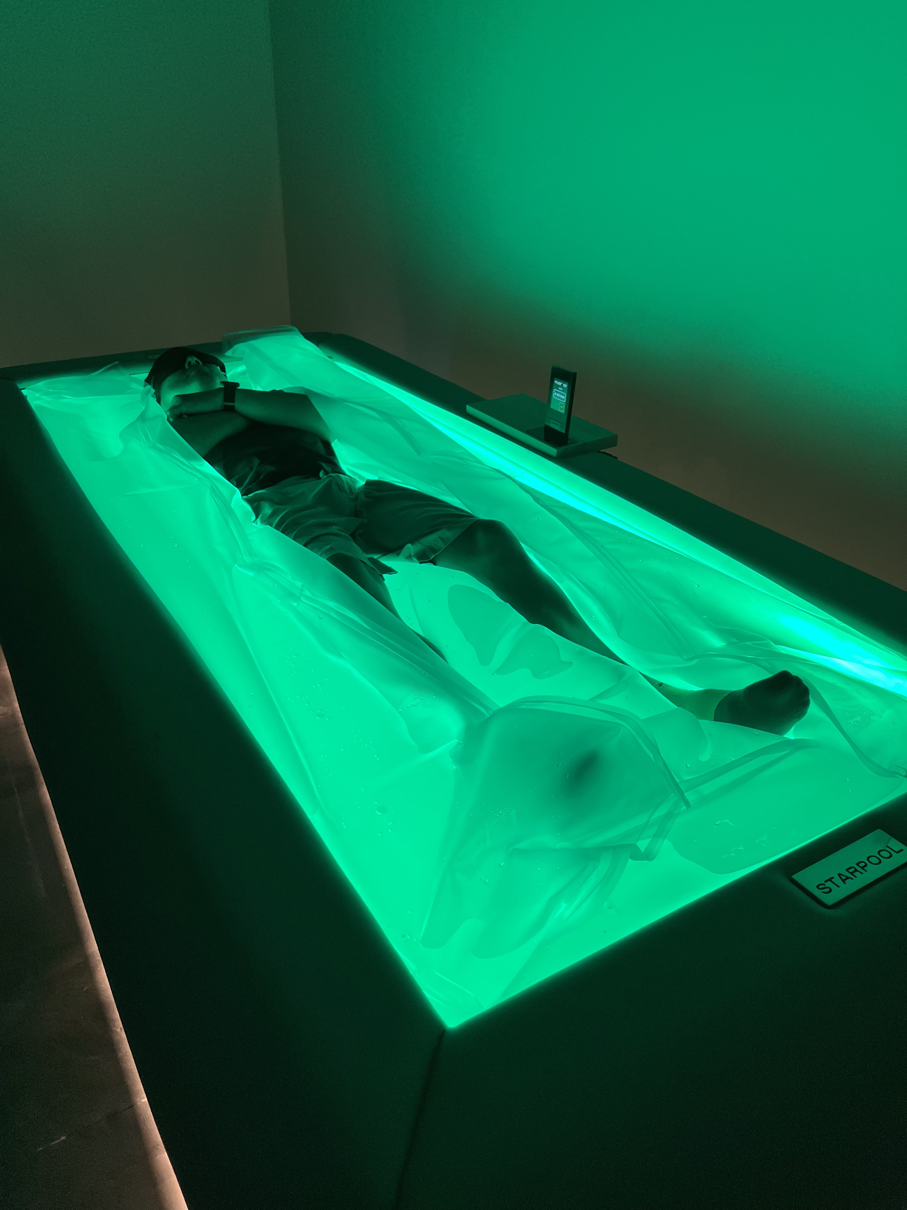 Client relaxing on Starpool dry float bed with green ambient lighting at Zivel